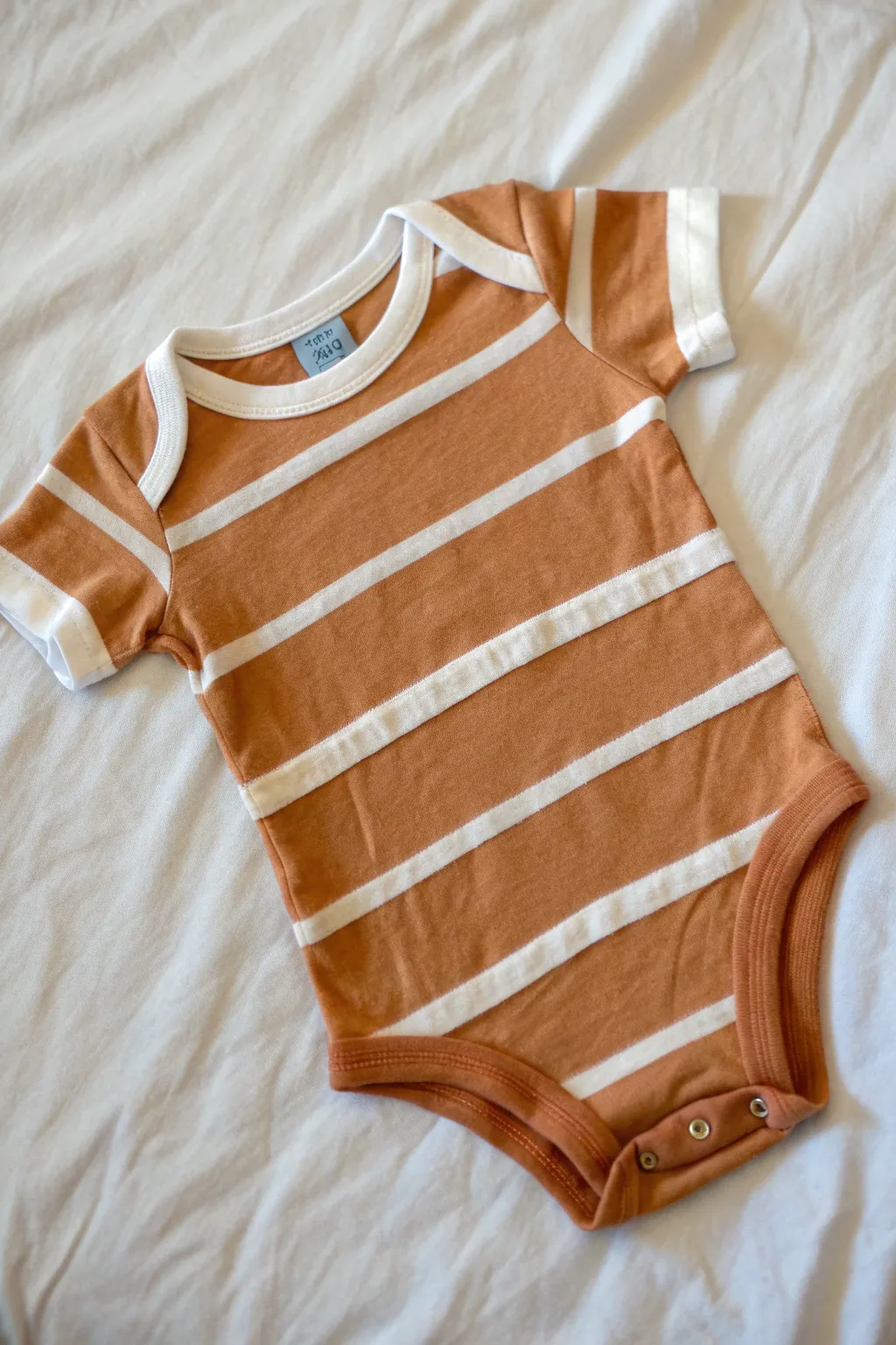 Crisp tape-resist stripes in progress on a baby onesie, clean lines and modern boho calm.
