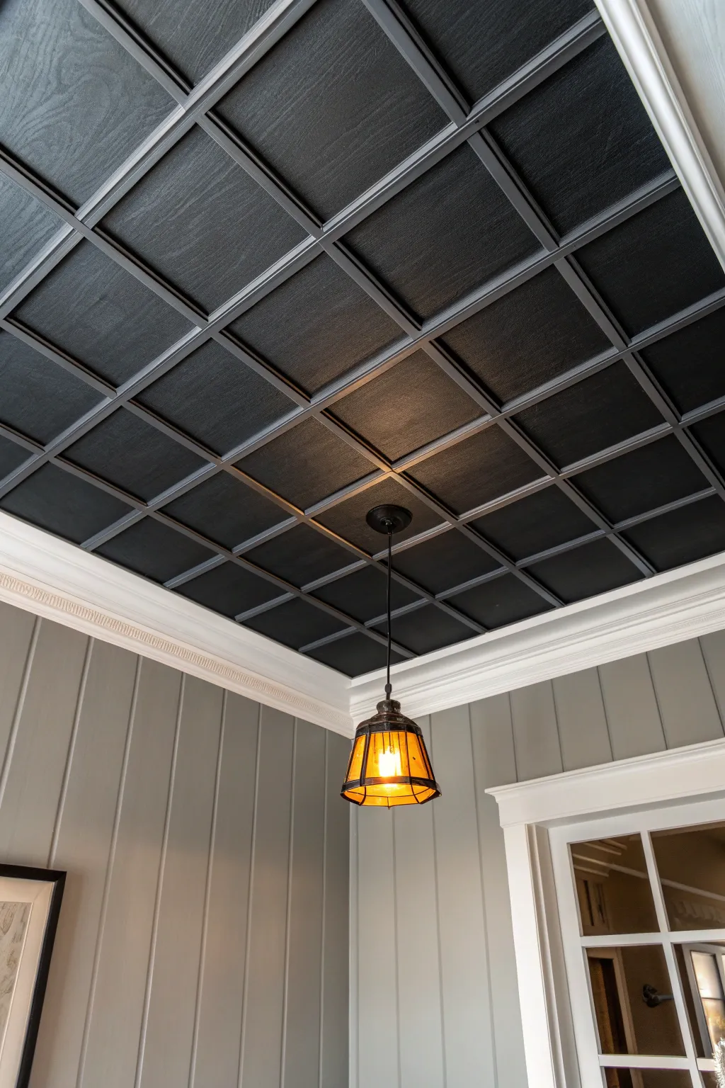 Moody charcoal ceiling tiles create a dramatic finish, softened by warm light and minimalist calm.