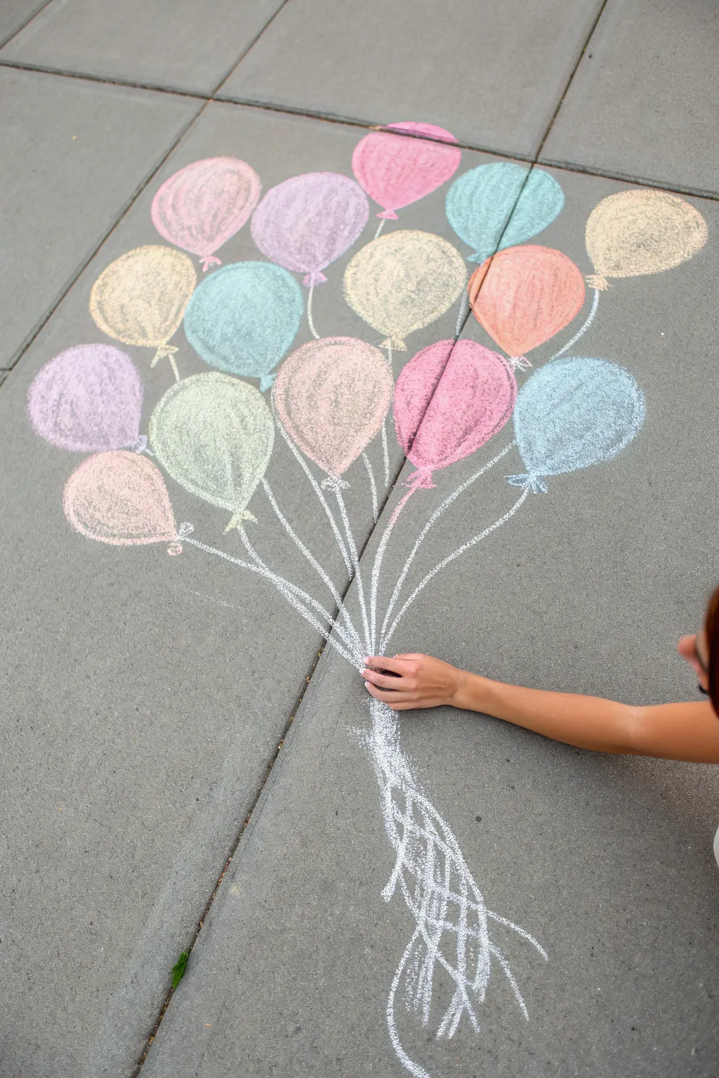 Playful balloon bouquet illusion: vibrant chalk balloons with strings ending in a real hand.