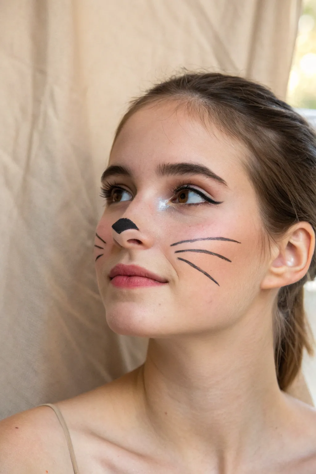 Minimal kitty cat face paint: tiny triangle nose, fine whiskers, and soft rosy blush.