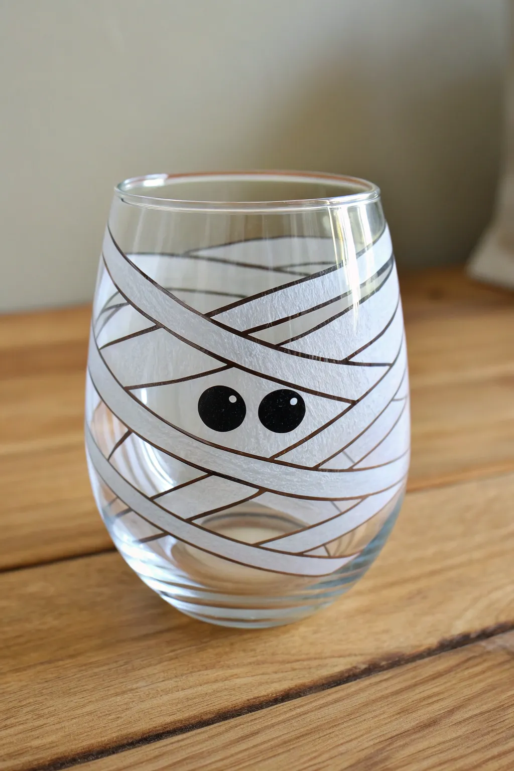 Paint a minimalist mummy glass: uneven white wrap stripes, soft gray shadows, peeking black eyes.