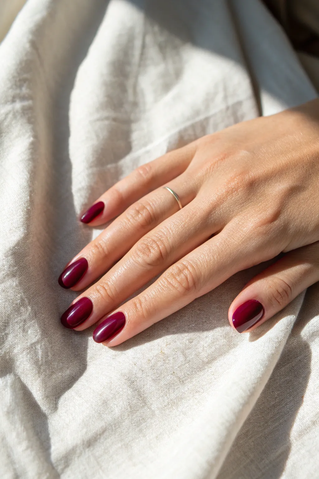 Glassy single-color nails in a rich shade, set against linen for a clean minimalist look