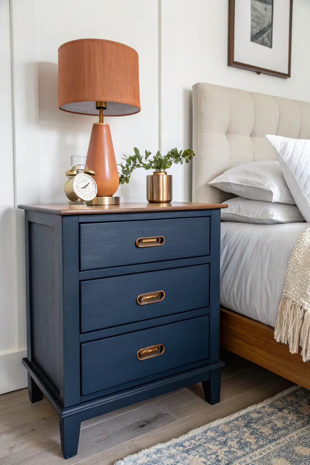 Moody navy statement nightstand with warm lamp glow and light bedding for bold contrast