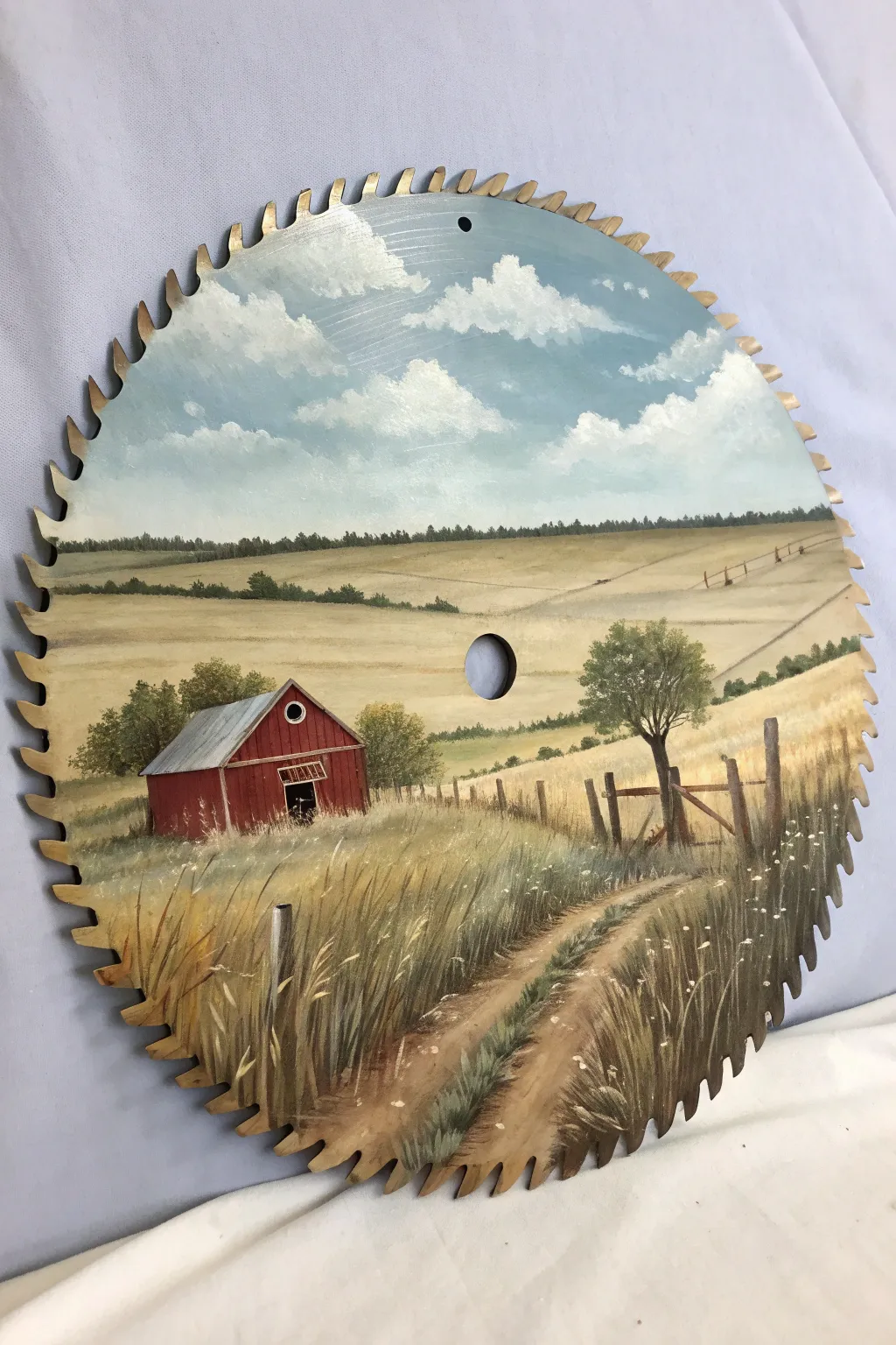 Rustic red barn painted on a saw blade, framed by steel teeth and airy field tones