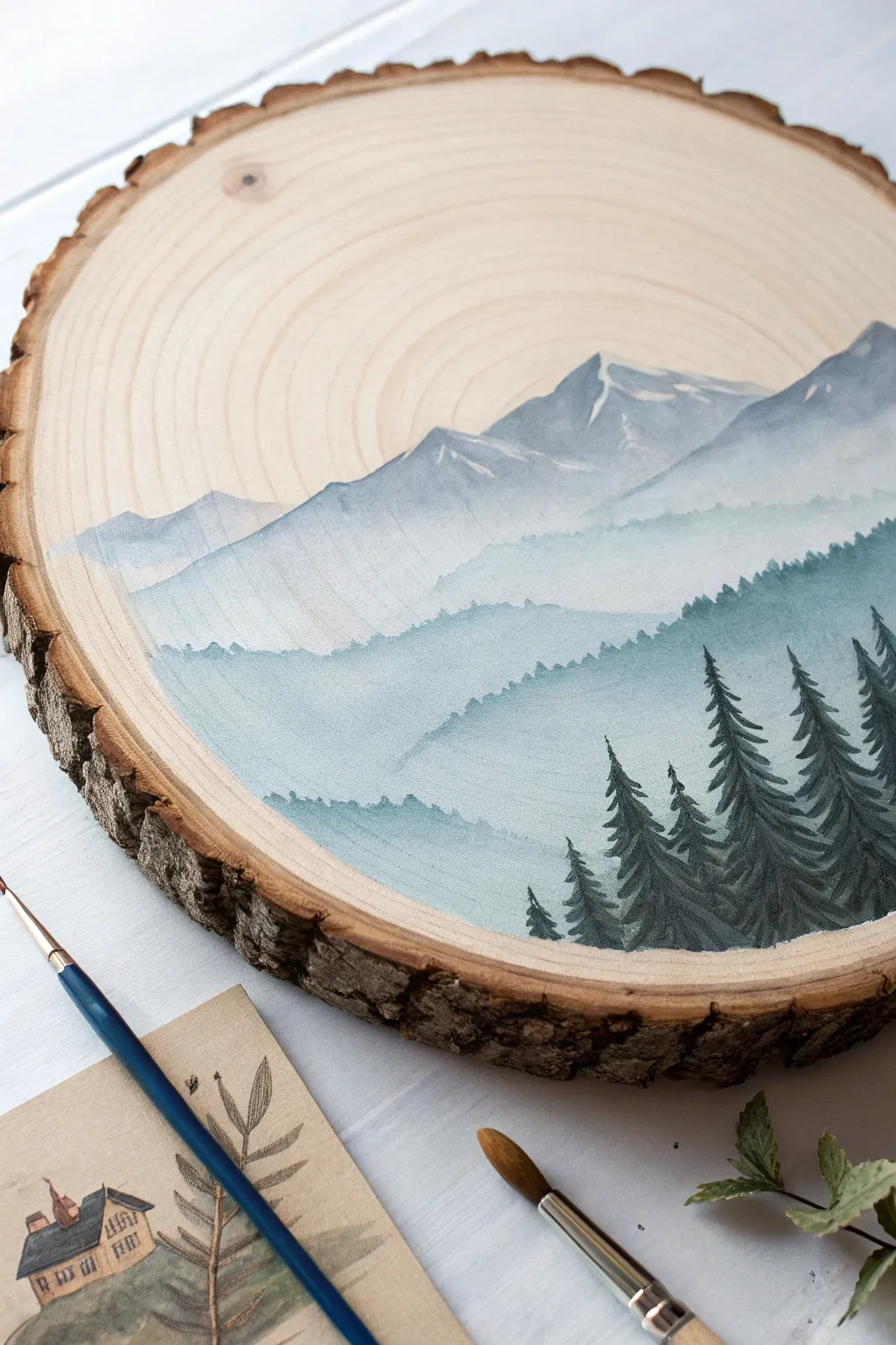 Minimal wood slice mountain painting with misty blues and natural rings framing the scene.
