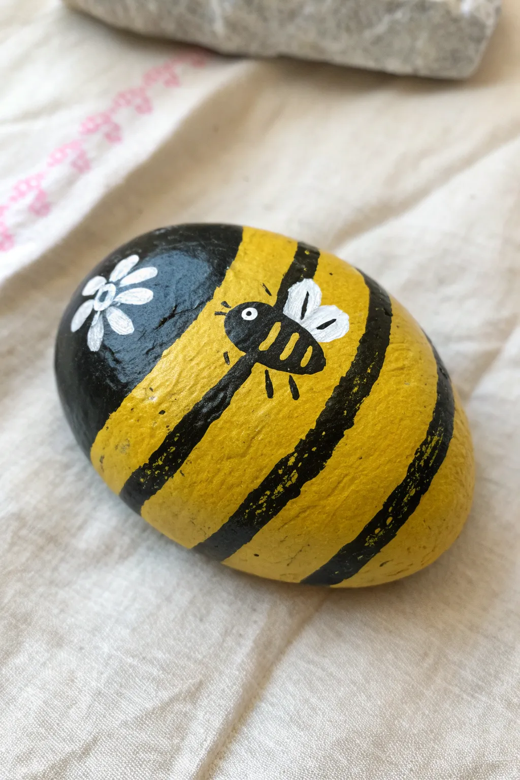 Bold bumblebee stripes on a long stone, a chic Scandinavian-boho rock painting idea.
