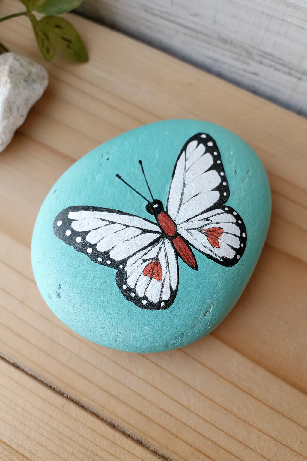 Bright teal base coat makes this simple butterfly rock painting pop in minimalist boho style