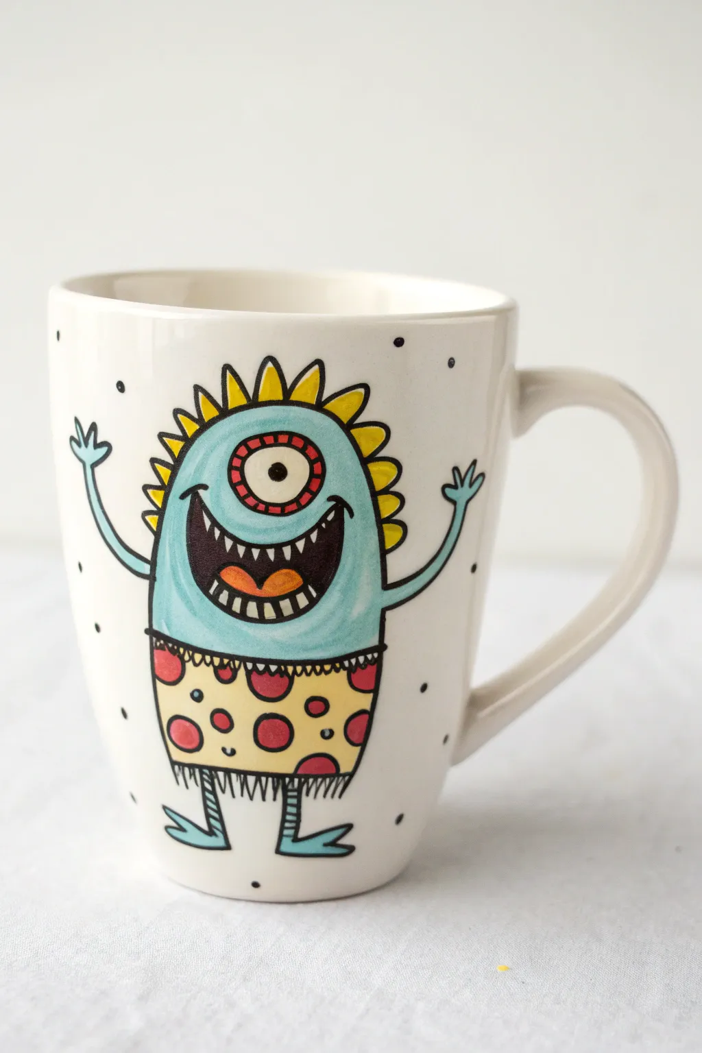 Goofy wraparound doodle monster mug with bold colors, shown front and handle side in clean minimal style