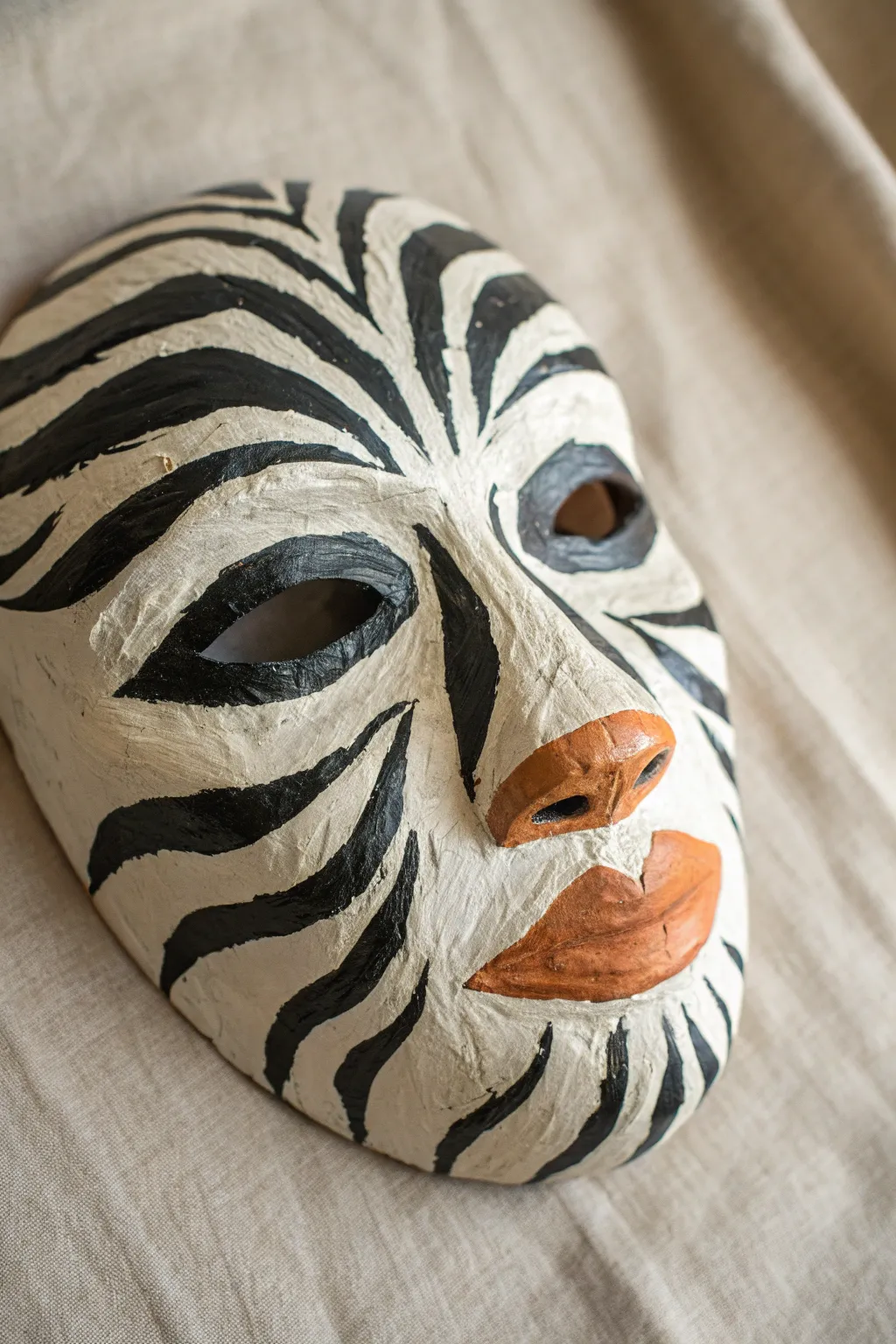 High-contrast striped plaster mask with a painted nose, celebrating handmade texture and bold color