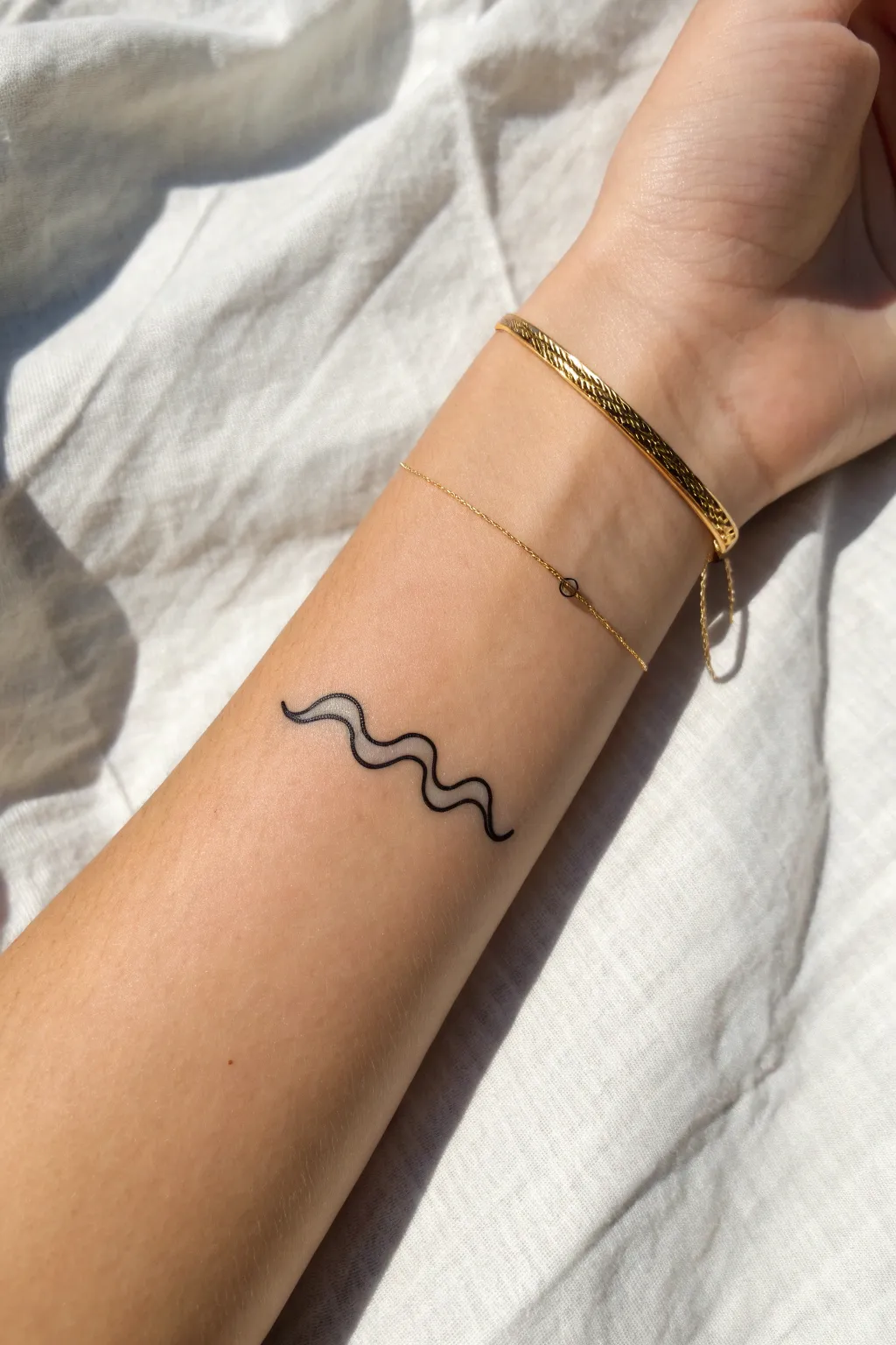 Single-line wave tattoo on the wrist, minimalist and calm with bold contrast and clean lines