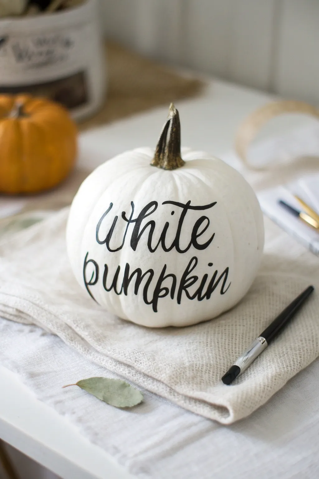 Minimalist white pumpkin with bold black hand lettering, styled with brush and sketch paper.