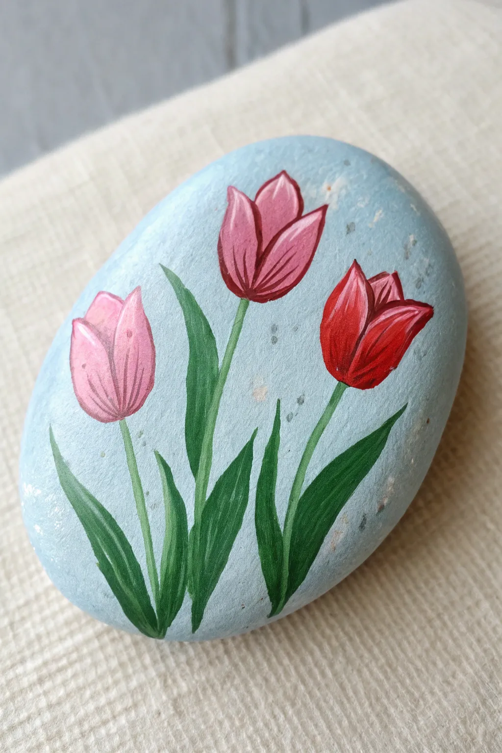 Simple tulip cluster rock painting in bold pinks and reds on a pale sky-blue base