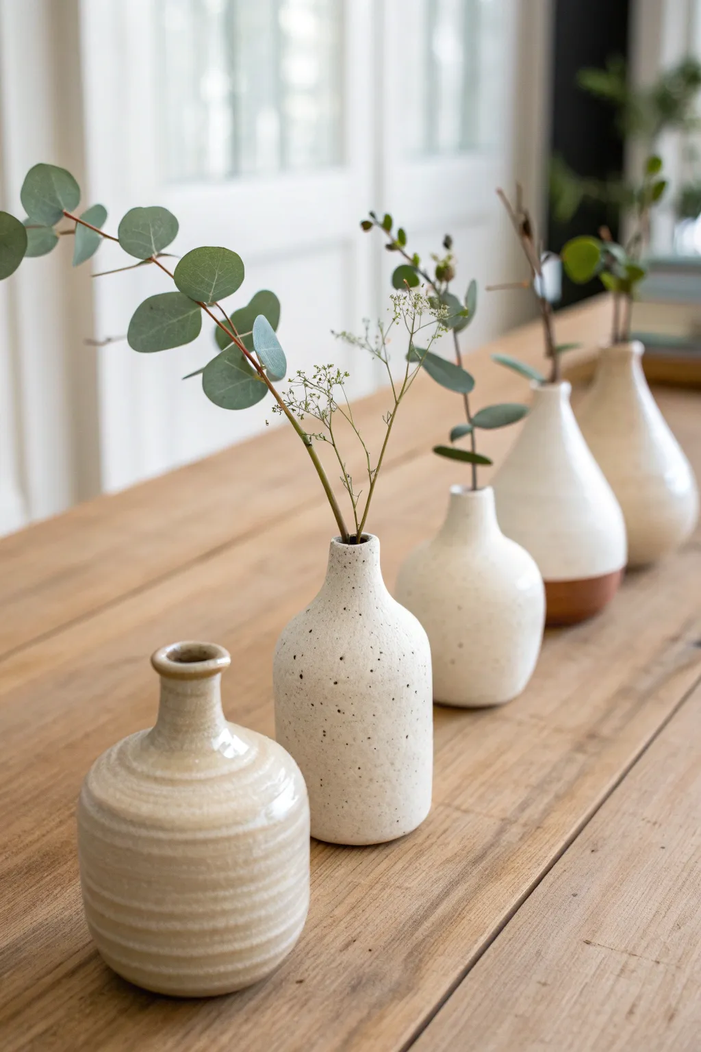 Mini bud vase collection in soft earthy tones, each holding one fresh stem, clean and calm.