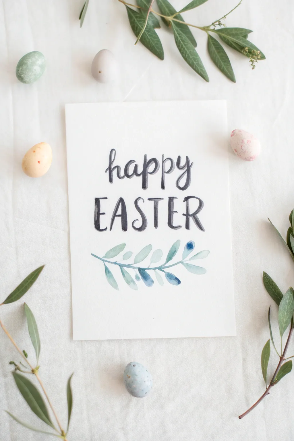 Happy Easter watercolor hand lettering with tiny pastel eggs and leafy sprigs, minimalist boho style