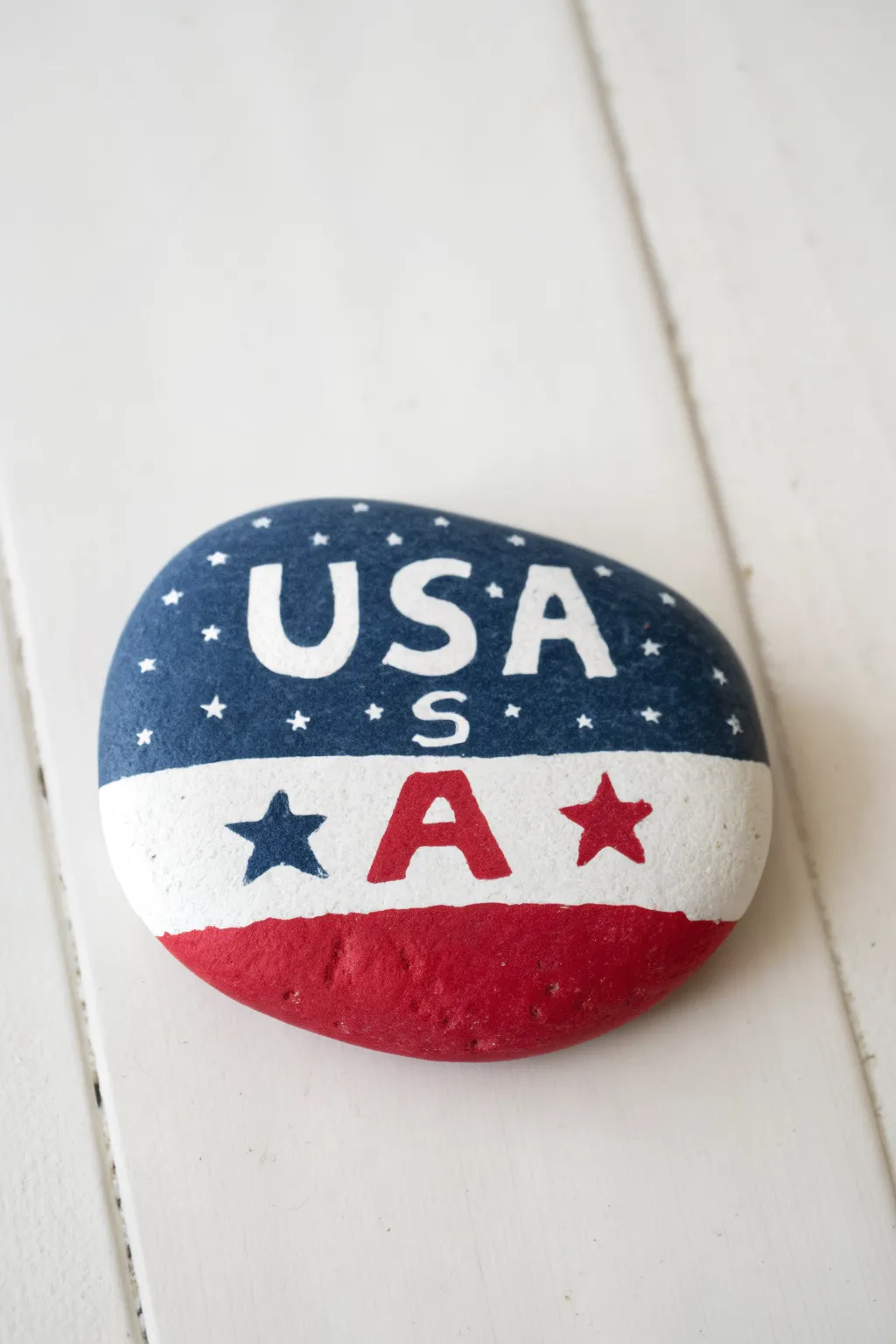 DIY painted rock with bold USA block letters in flag patterns, clean minimalist patriotic decor