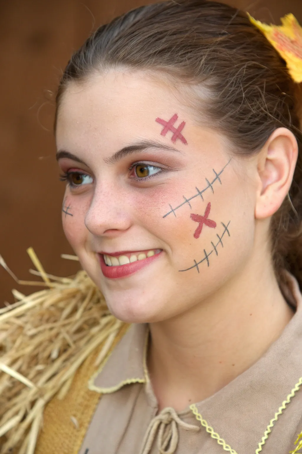 Friendly scarecrow face paint with stitched smile, rosy cheeks, and straw accents for fall festivals