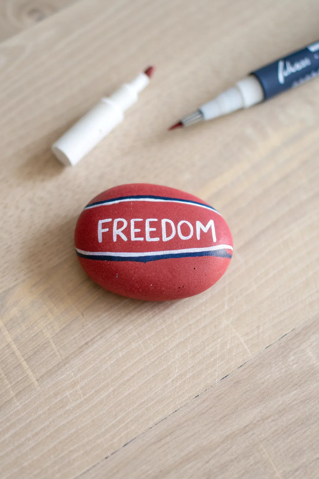 Patriotic rock painting: red stone with crisp white hand-lettering in minimalist boho styling