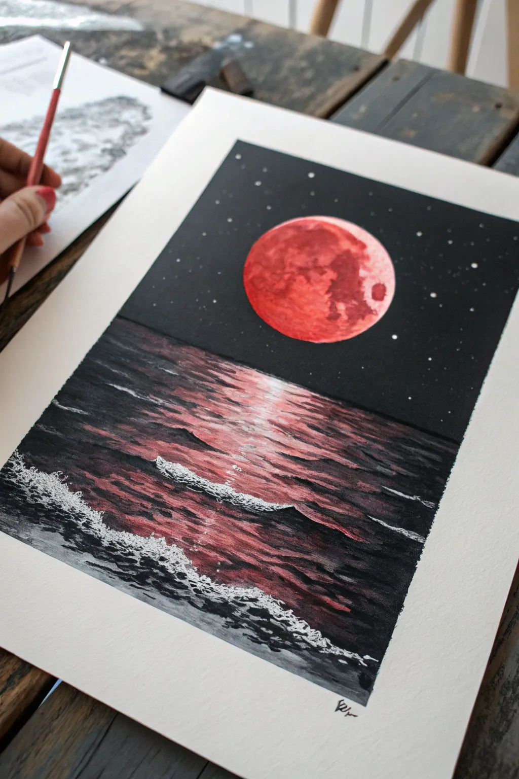 A bold red moon over an inky sea, with a shimmering crimson path across the waves