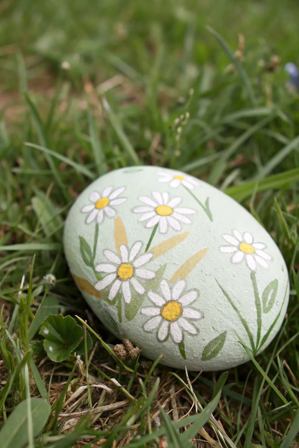 Hand-painted daisy river rock nestled in fresh grass, simple, sunny, and beautifully minimal.