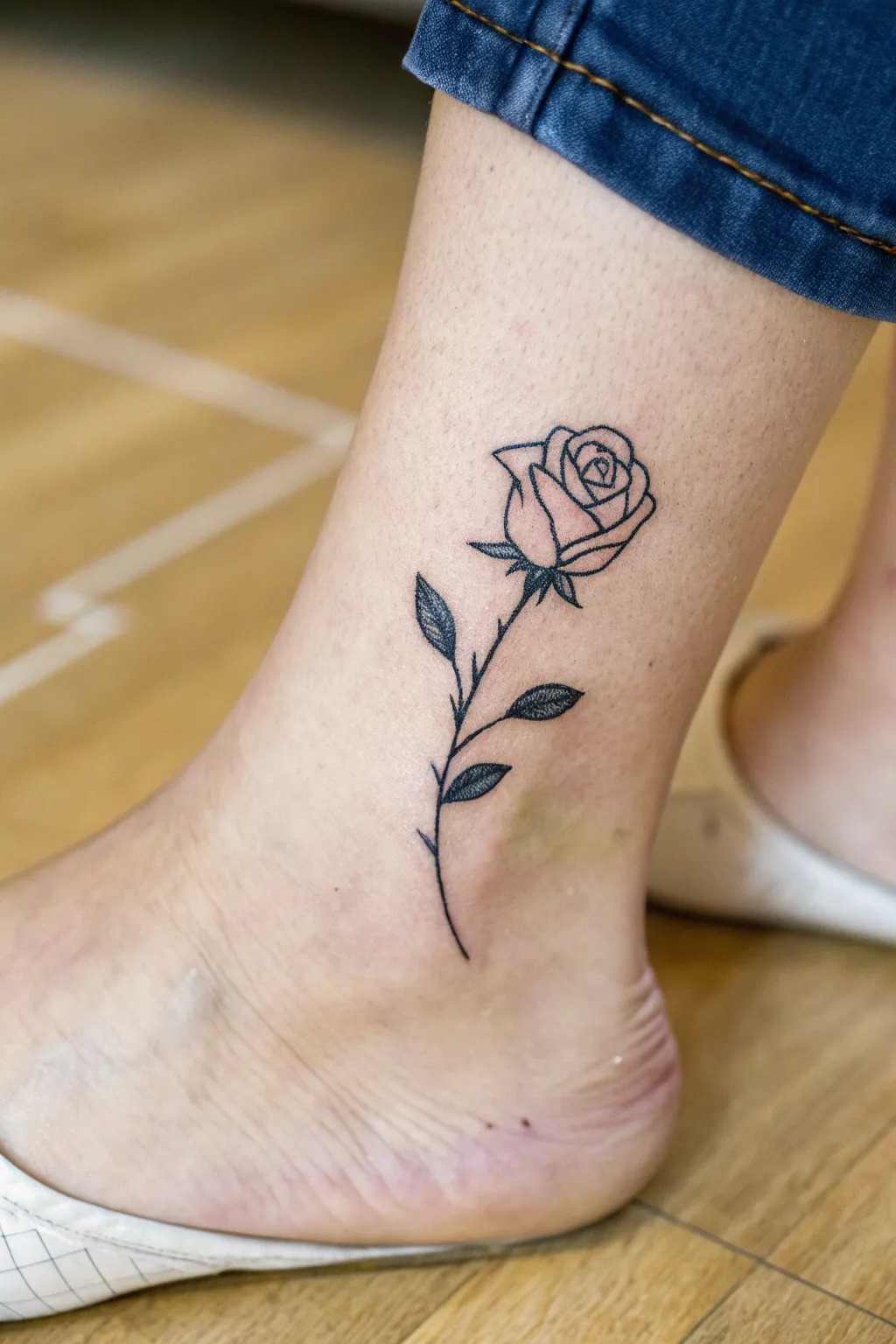 Tiny rosebud tattoo with two leaves, crisp fine lines and a calm minimalist vibe for everyday elegance