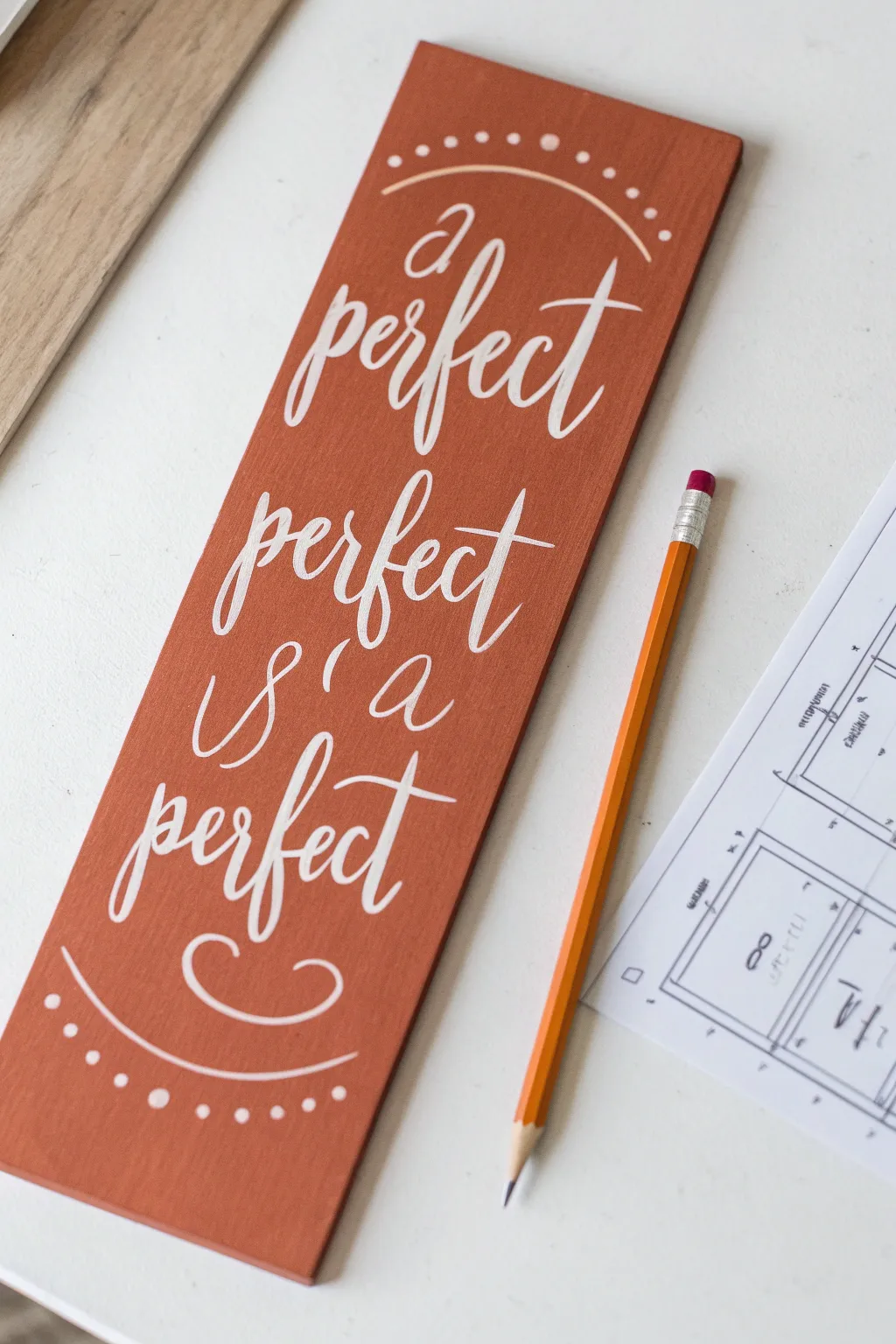 Minimal wood quote plaque with hand lettering practice strokes and a simple layout sketch