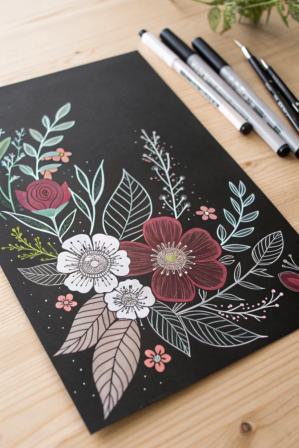 Black paper florals with crisp opaque highlights, made with acrylic paint pens on a minimal desk.