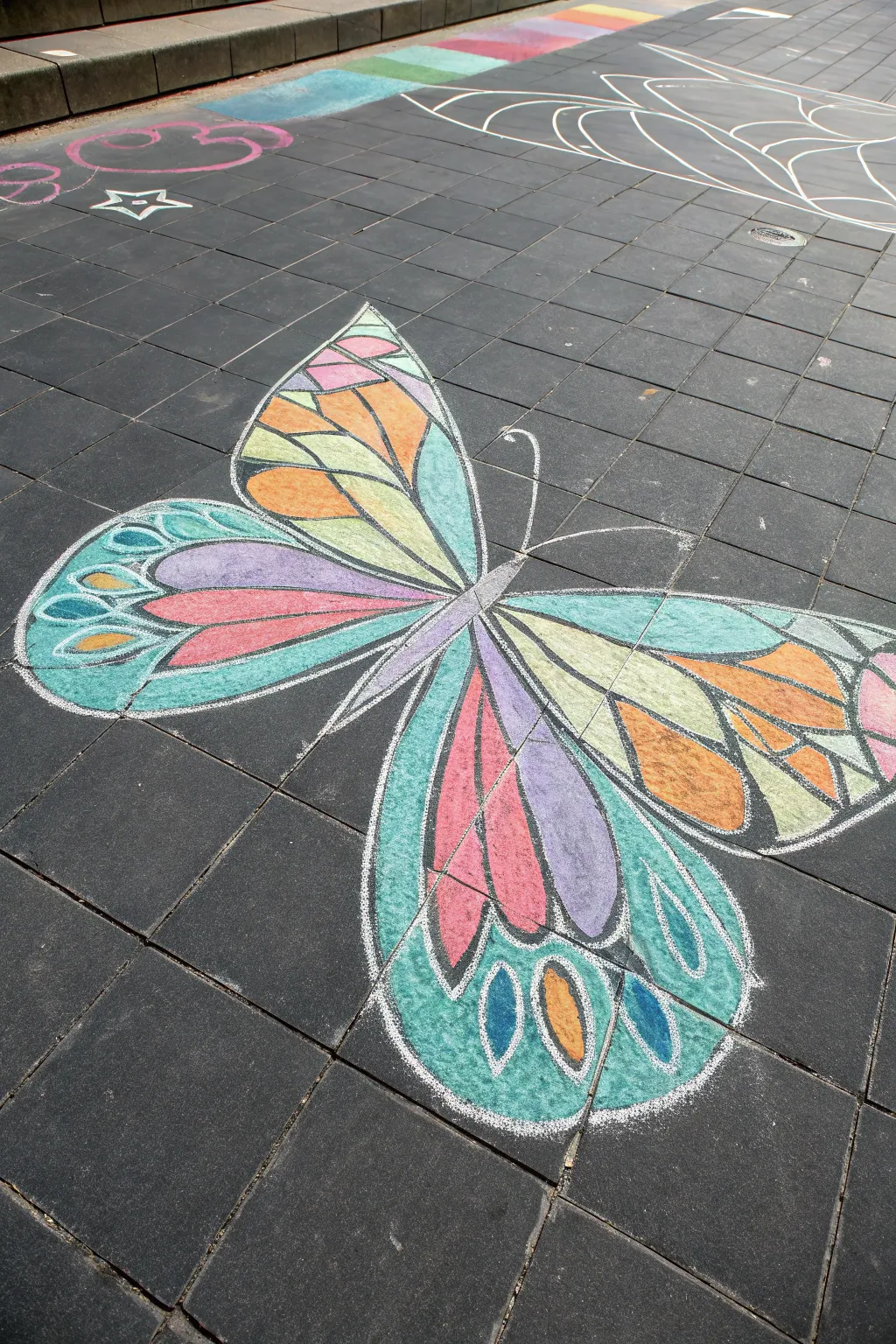 Butterfly stained-glass chalk art with tape resist lines, bright color on dark pavement.