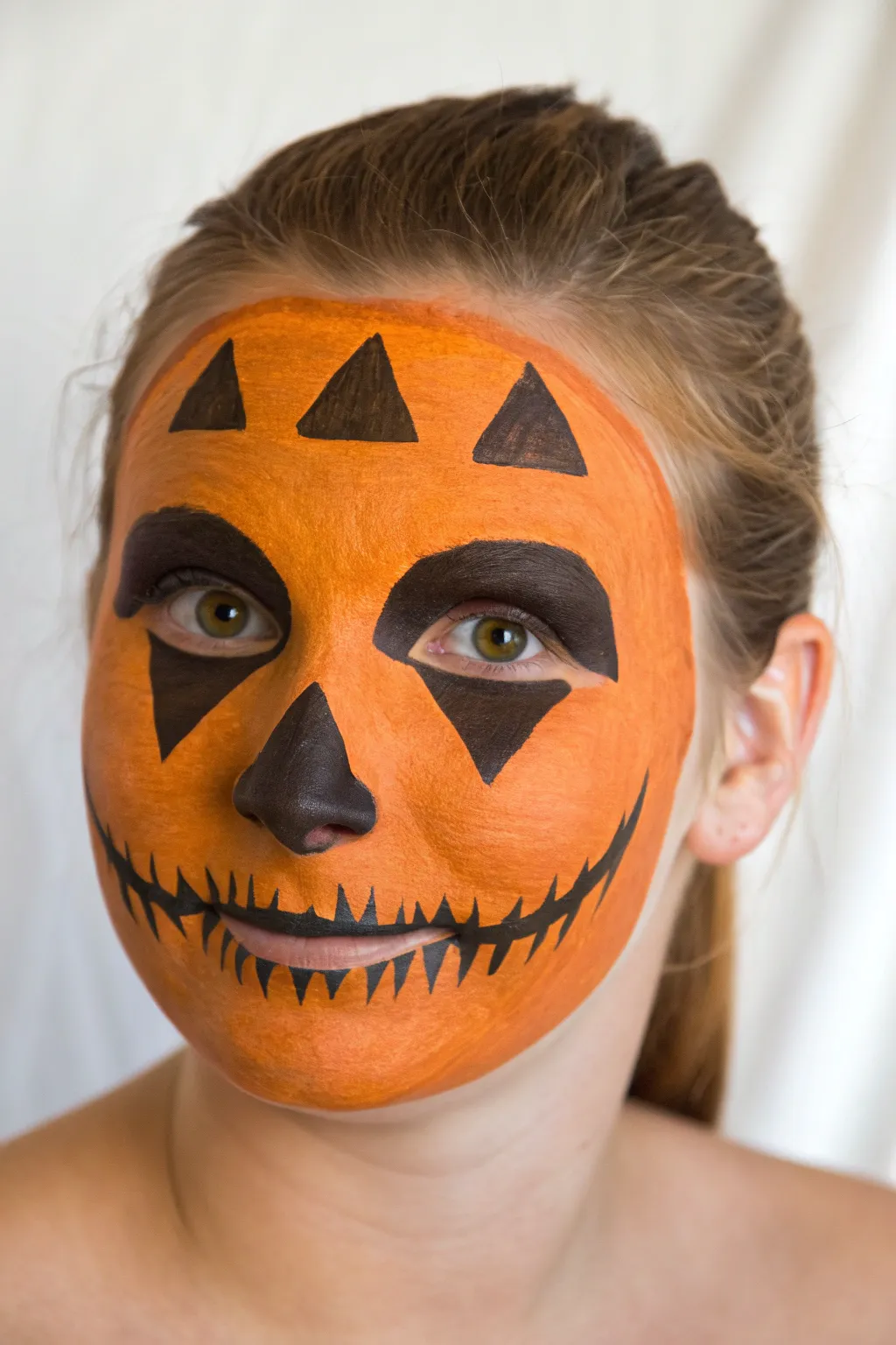 Bold jack o lantern full face paint with matte orange base and graphic black carved features