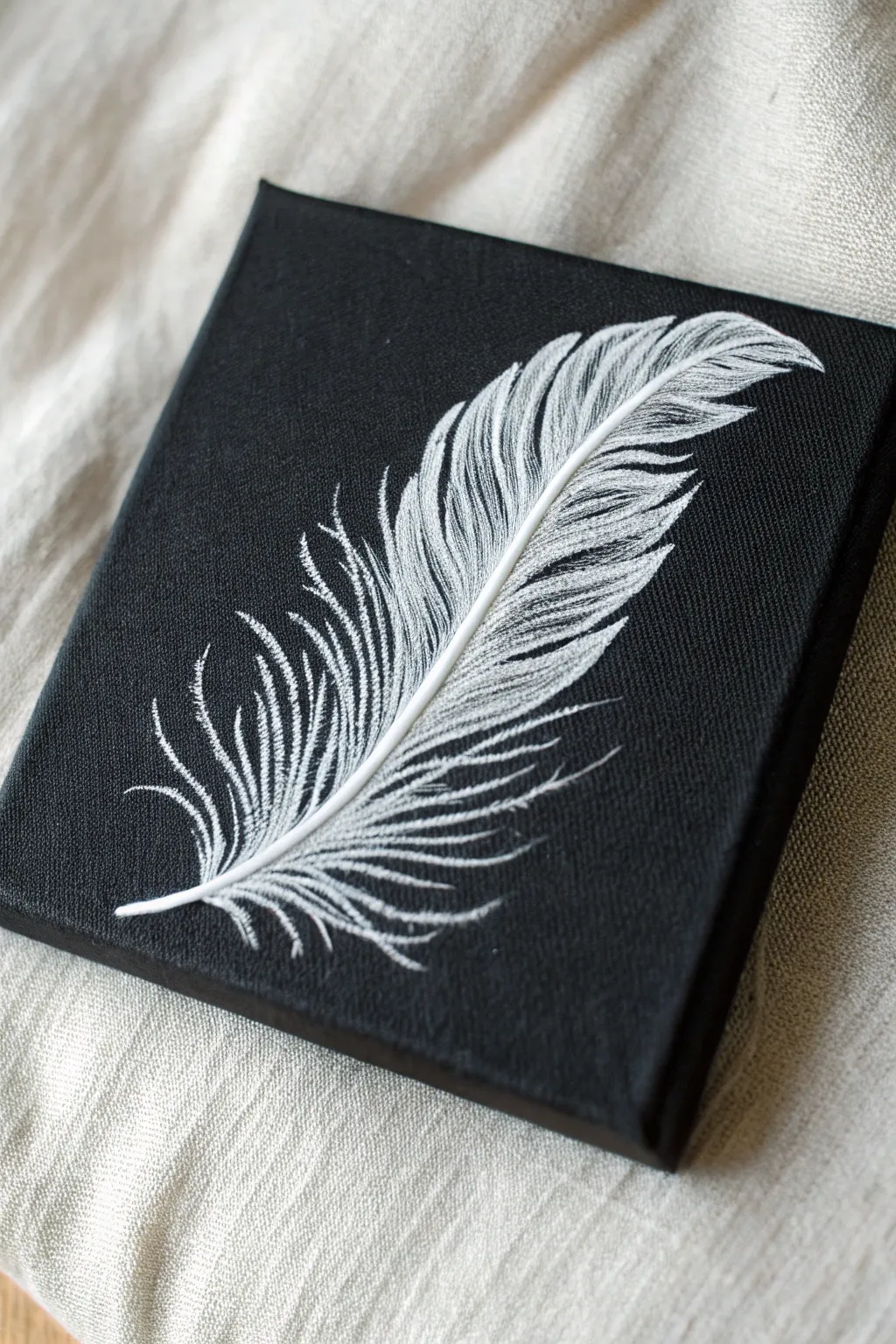 Mini black canvas with a single white feather, minimal and airy for easy ink-style painting.
