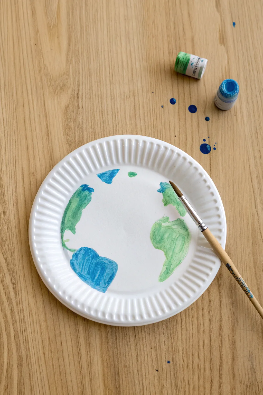 Easy paper plate Earth painting: bold blues and soft greens on a clean, minimal tabletop.