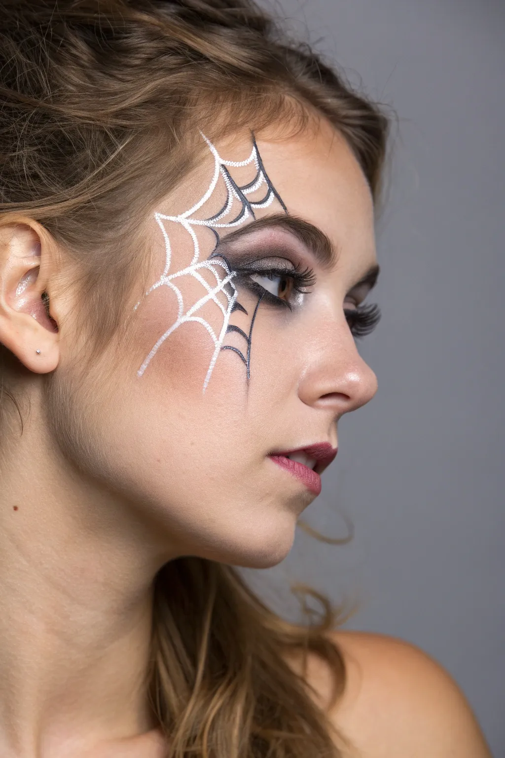 Minimalist spiderweb corner face paint with crisp linework and a tiny hanging spider for Halloween