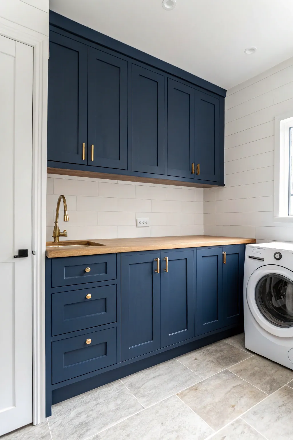 Deep blue laundry cabinets steal the show against soft neutral walls and simple brass pulls.
