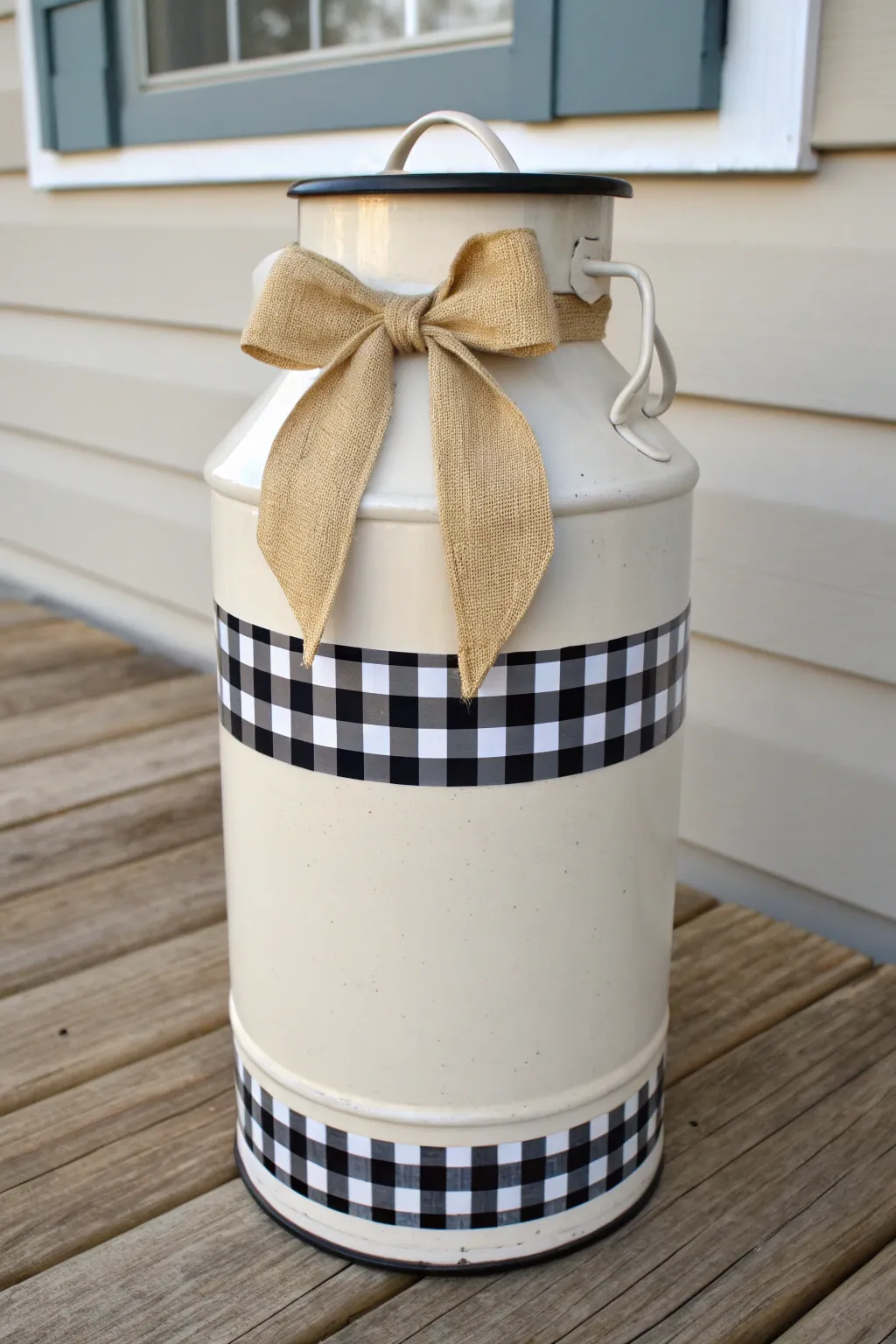 Warm white milk can with bold buffalo check band and linen bow, styled for a cozy porch