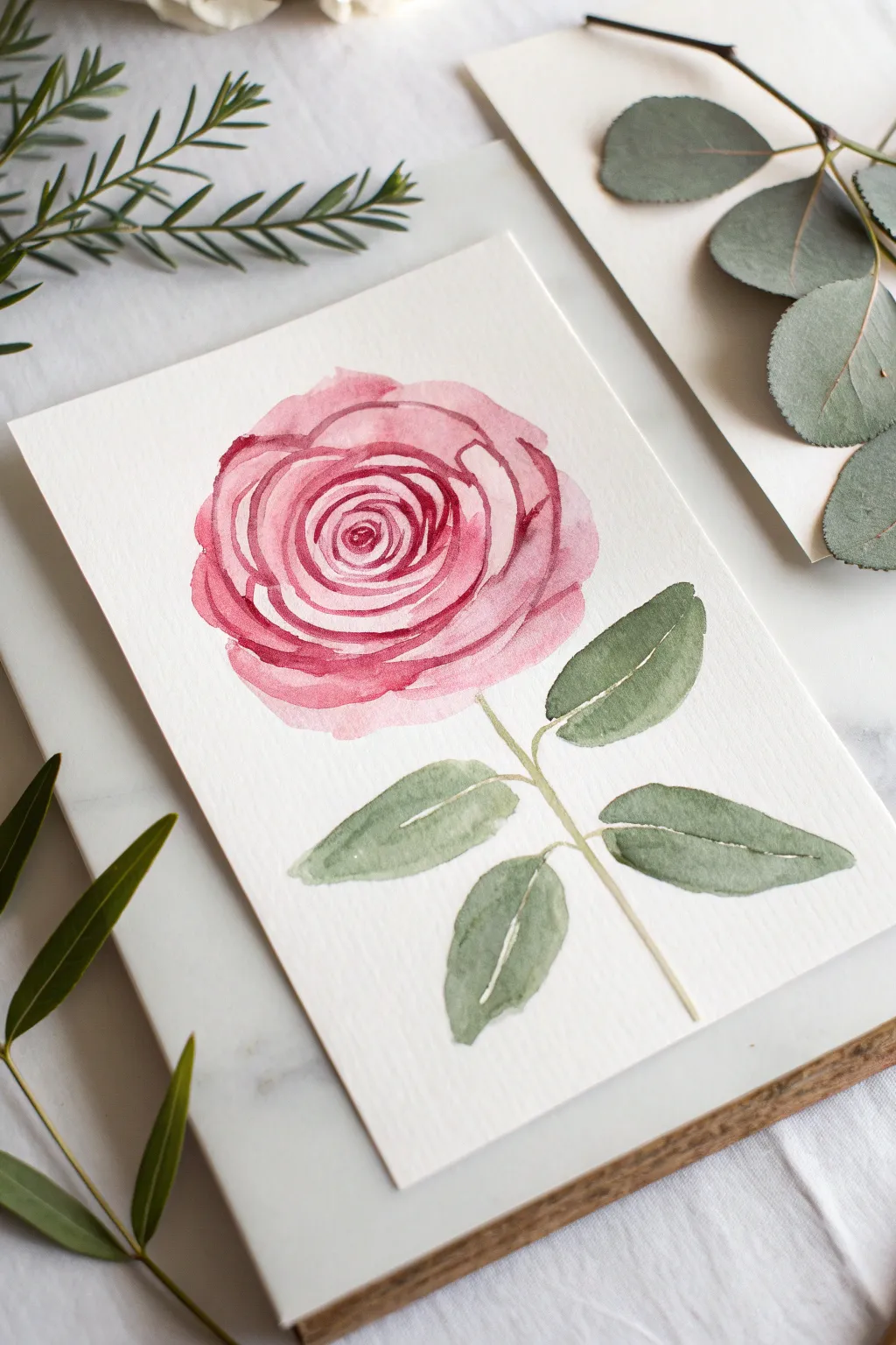 Easy spiral-stroke pink rose painting idea with soft green leaves on a clean minimalist backdrop