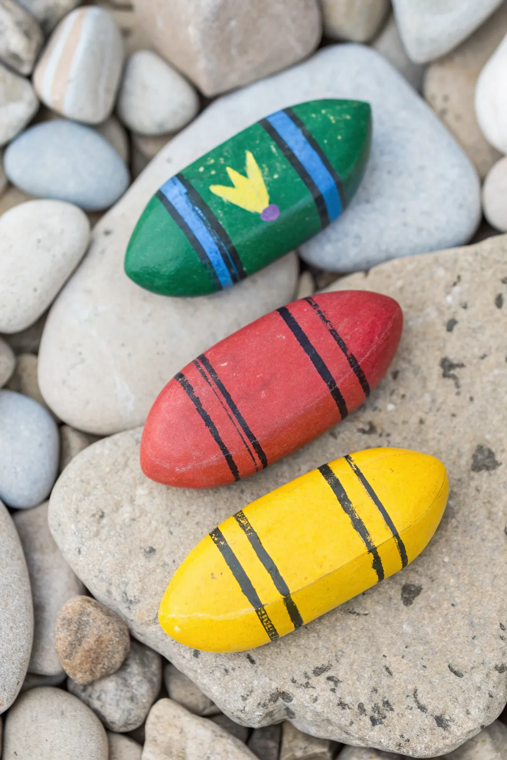 Three crayon-painted rocks in bright classroom hues, minimalist and boho, perfect for school crafts