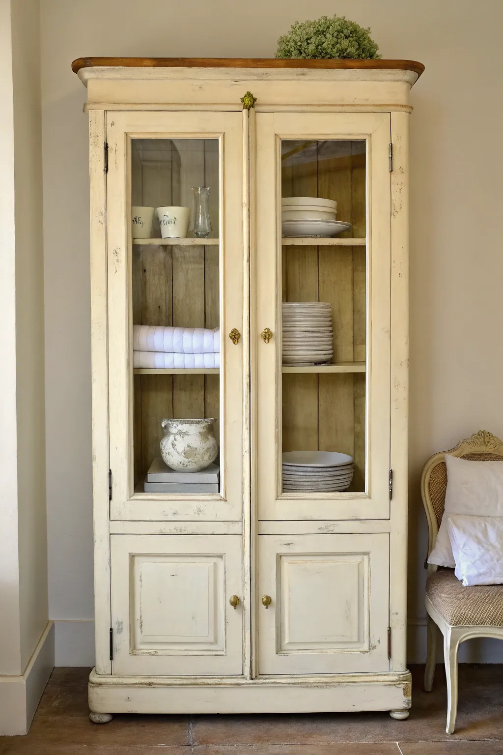 Soft cream glass-front cabinet with gentle patina, perfect for showcasing vintage dishes and linens.