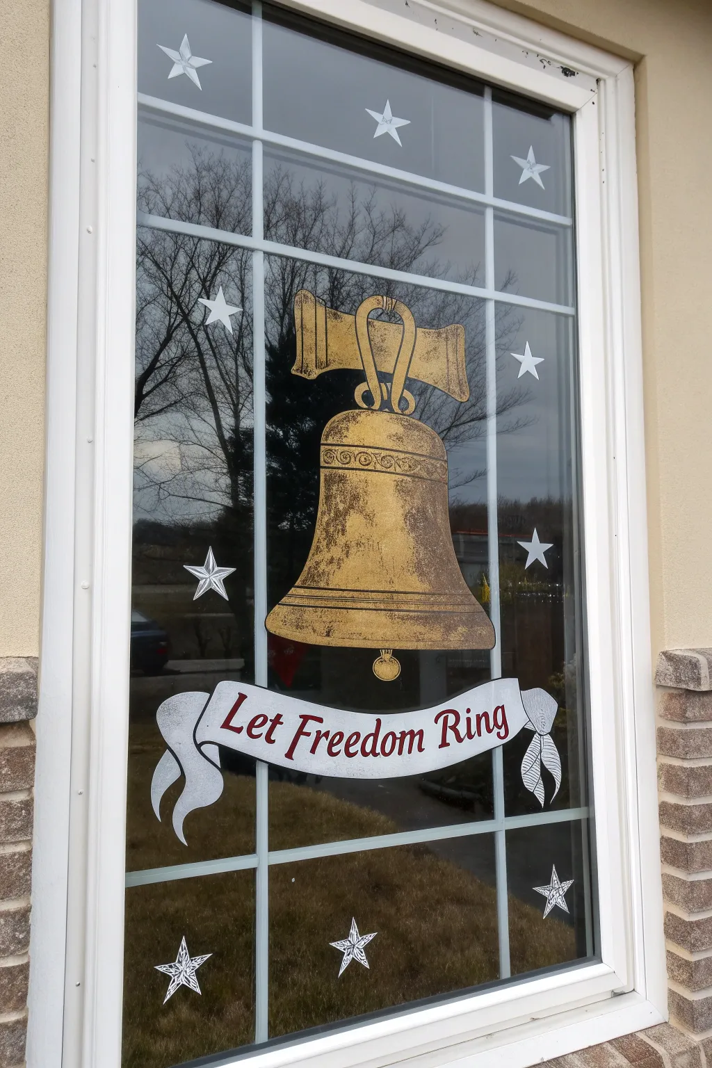 Minimalist Liberty Bell window painting in warm gold with banner and stars, bold July contrast.