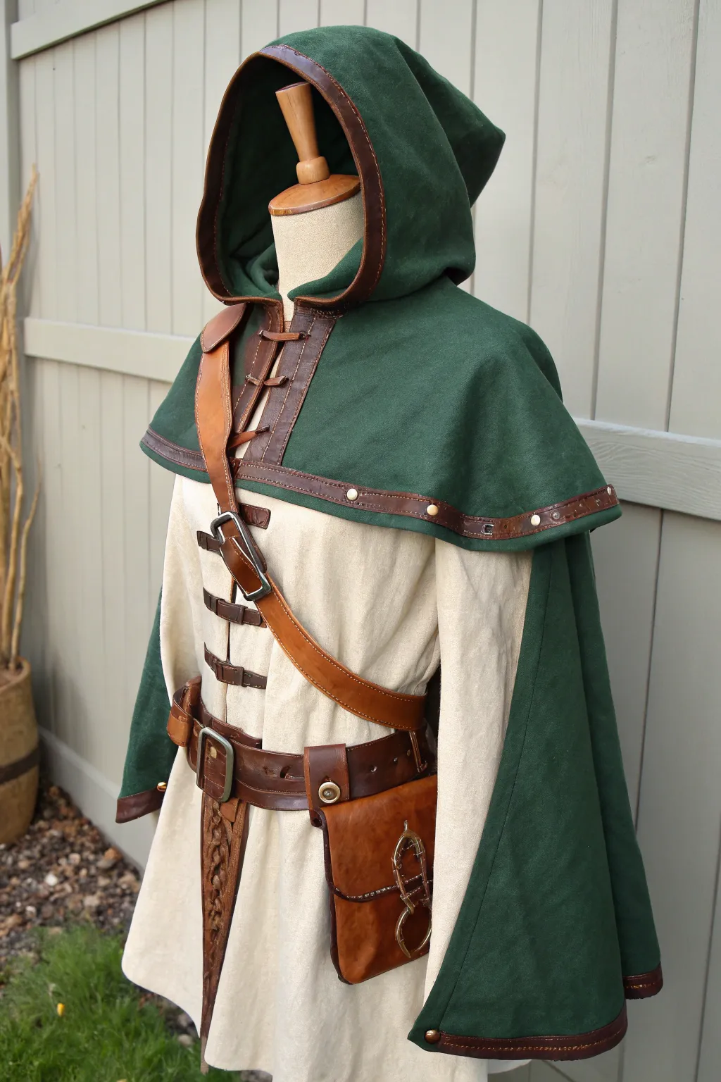 Fantasy ranger layers with hooded capelet, belts and pouch straps in bold forest and clay tones.