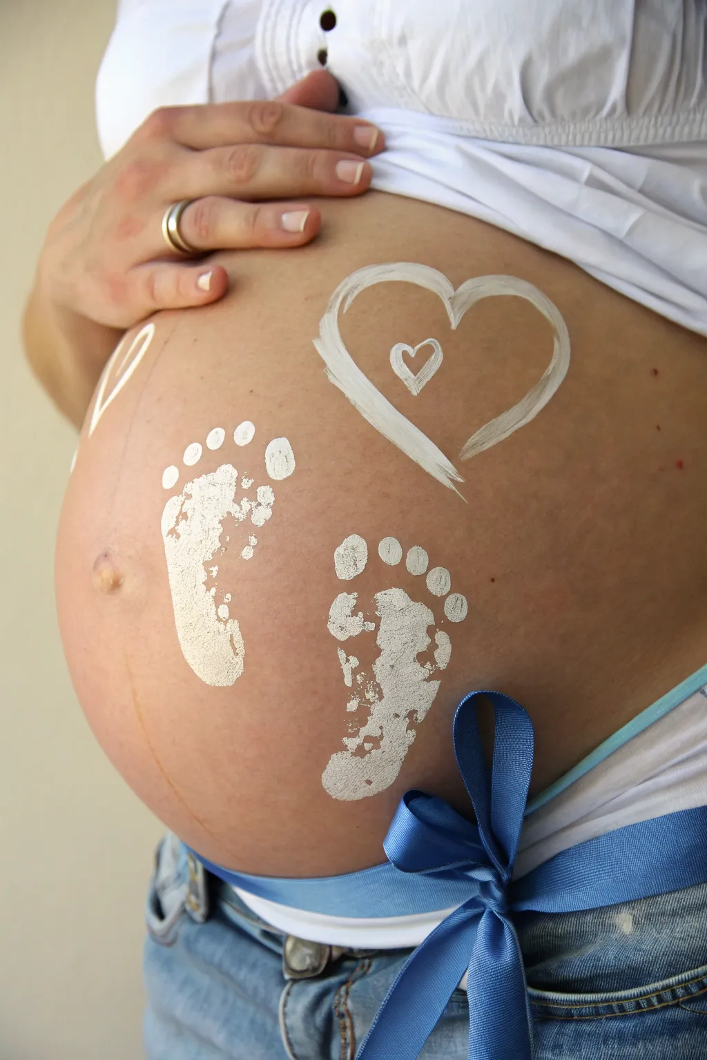 Tiny baby boy feet kicking illusion belly art with soft shadows and a bold blue heart accent
