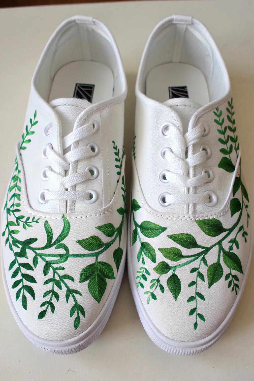 DIY botanical vines on canvas sneakers, bold emerald leaves on crisp white for cozy minimal style.