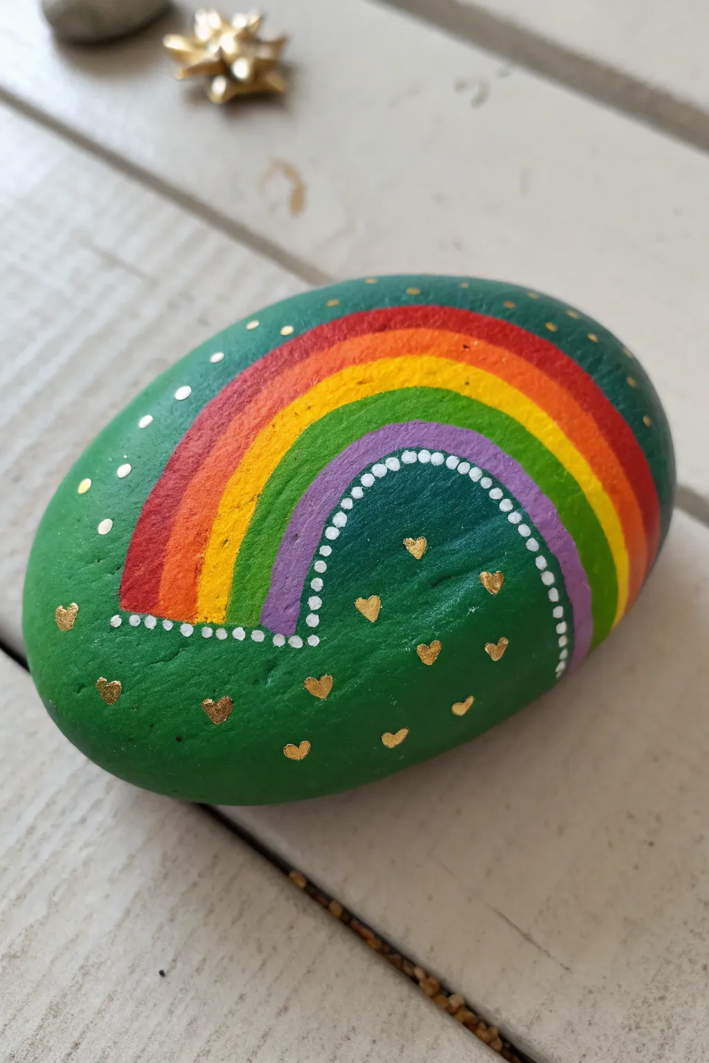 Bold rainbow and pot of gold on a deep green rock, minimalist boho craft with striking contrast.