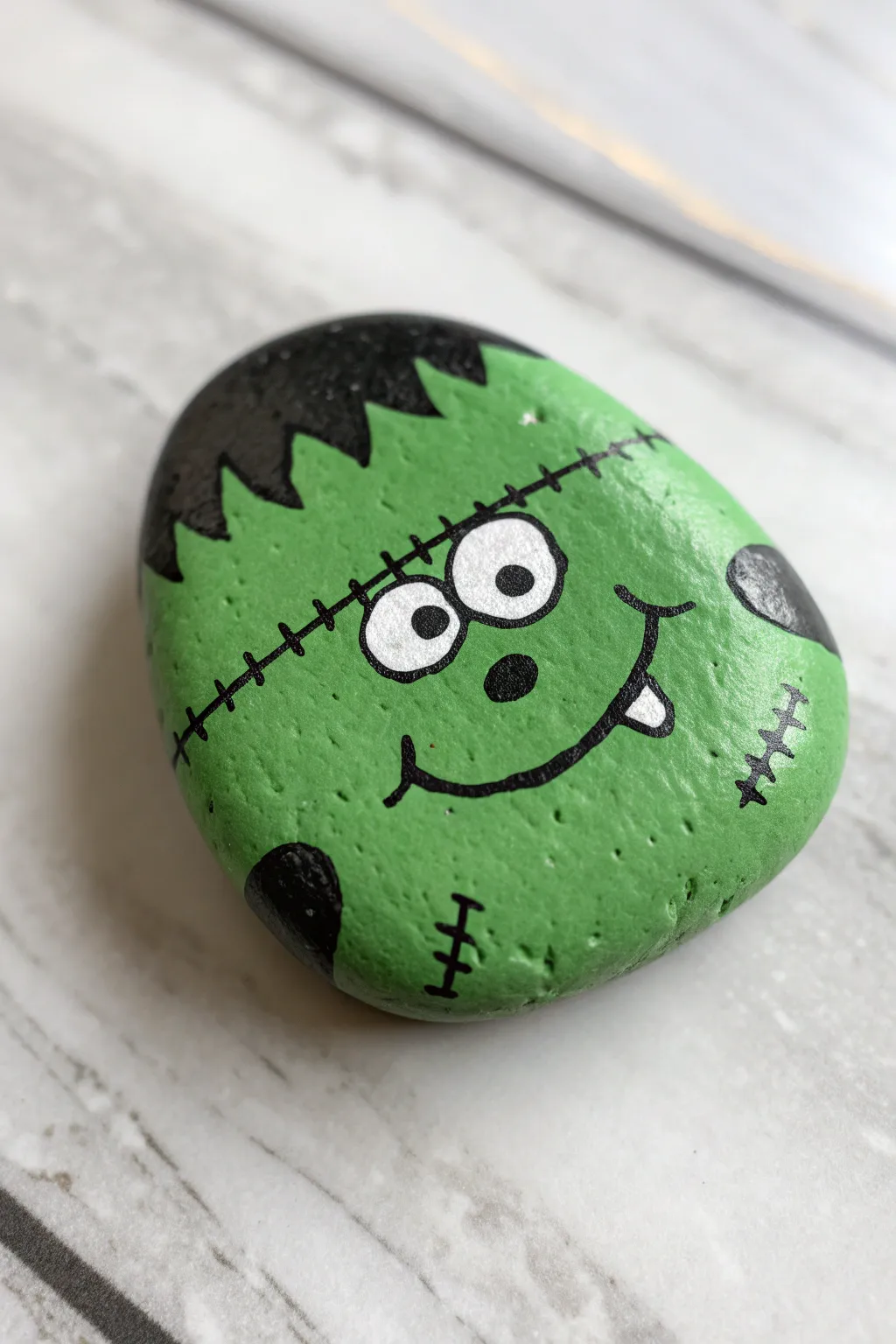 Cute Frankenstein painted rock with stitched smile, bold green pop, perfect Halloween DIY decor.