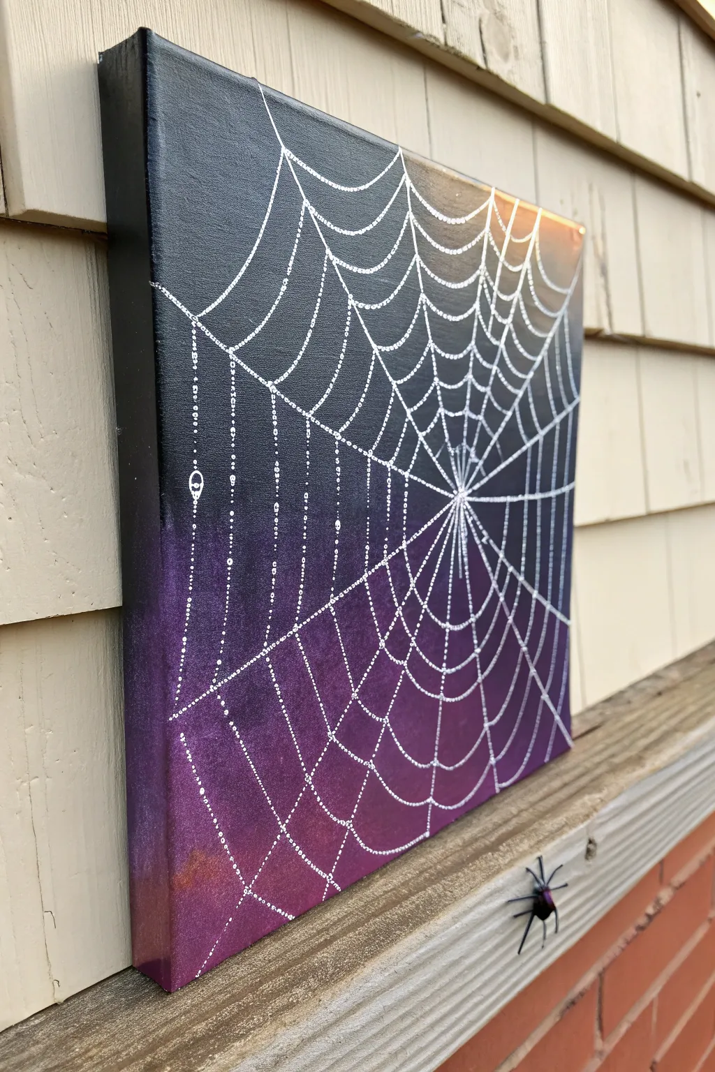 Minimalist spiderweb corner painting on a dark canvas with a tiny spider and silver highlights