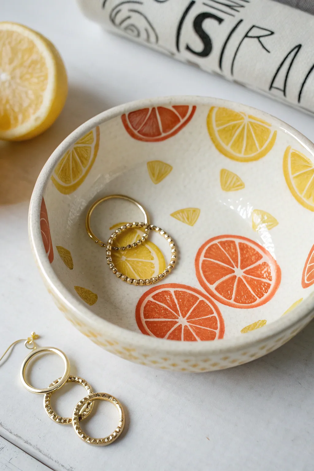 Minimal citrus-slice jewelry dish with bold color pops and gold hoops, shot overhead