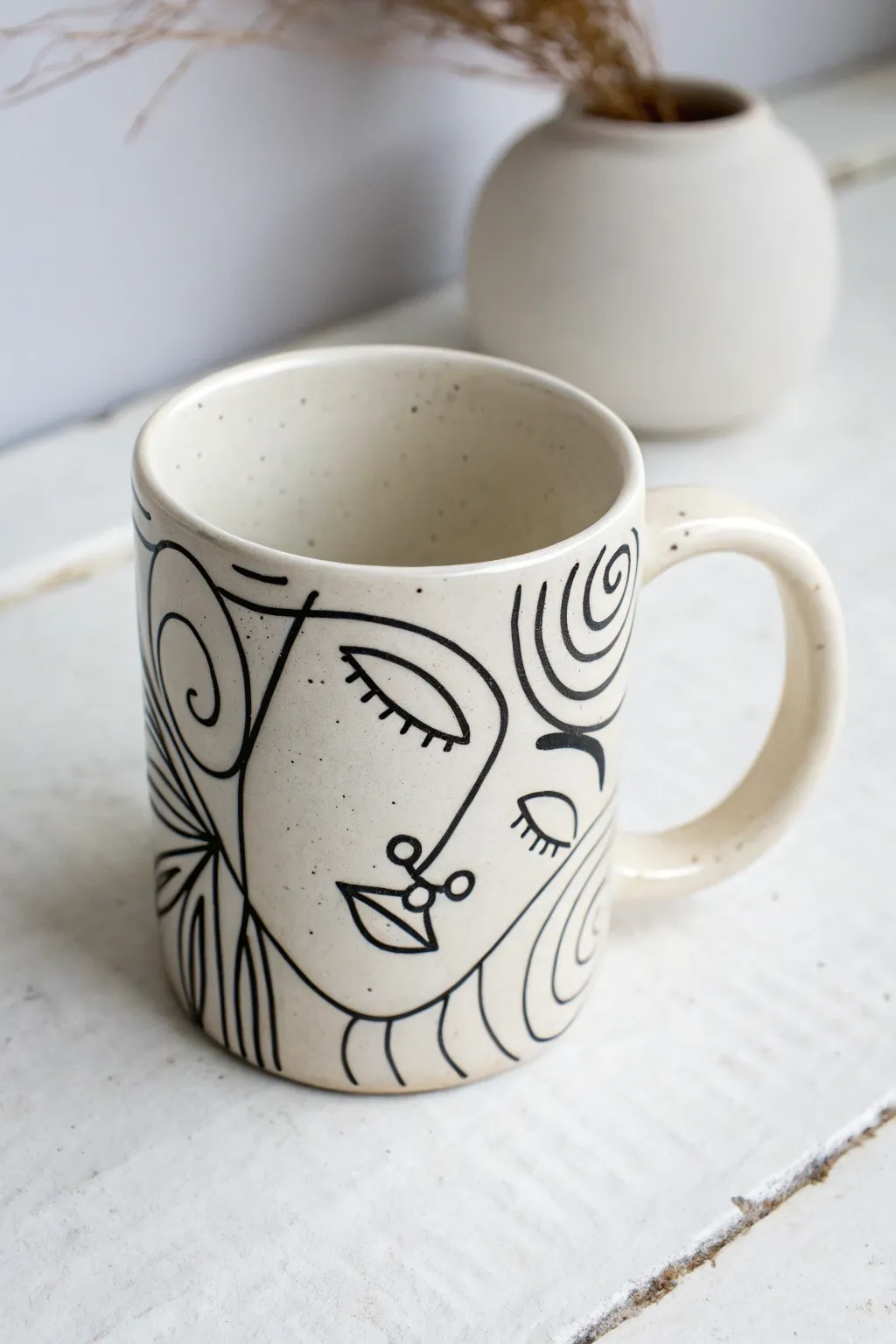 Minimal black line art face on a white mug, crisp contrast and serene Scandinavian styling.