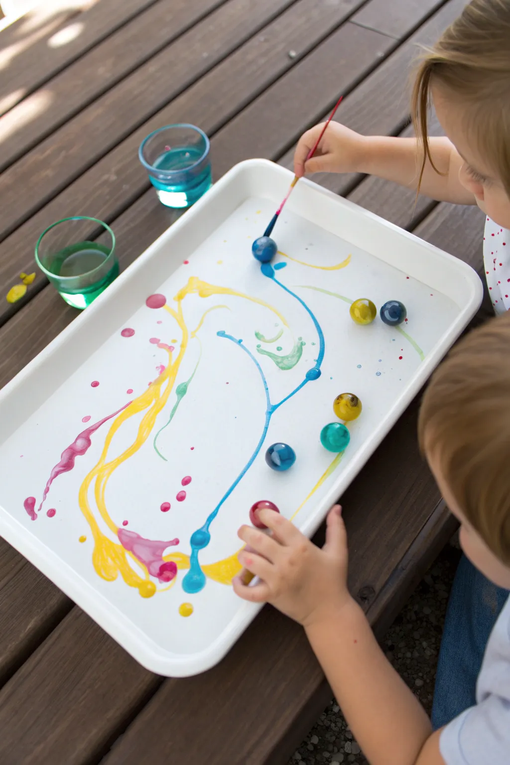 Marble roll painting: bold paint puddles and rolling marbles create mesmerizing track art for kids.
