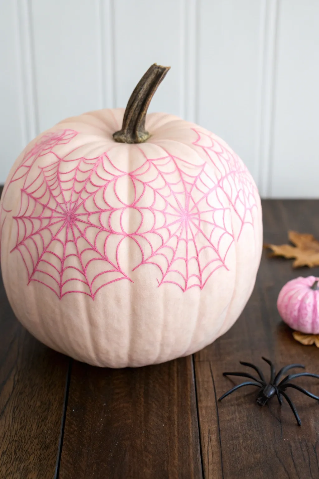 Spooky-sweet blush pumpkin with hot pink webs and one tiny black spider on dark wood.