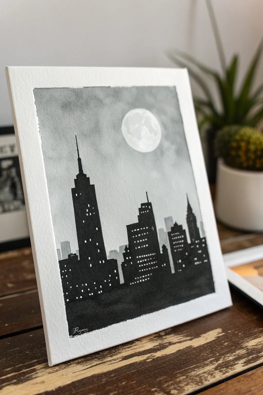 Moody black and white skyline silhouette with glowing windows and a soft moonlit haze behind.