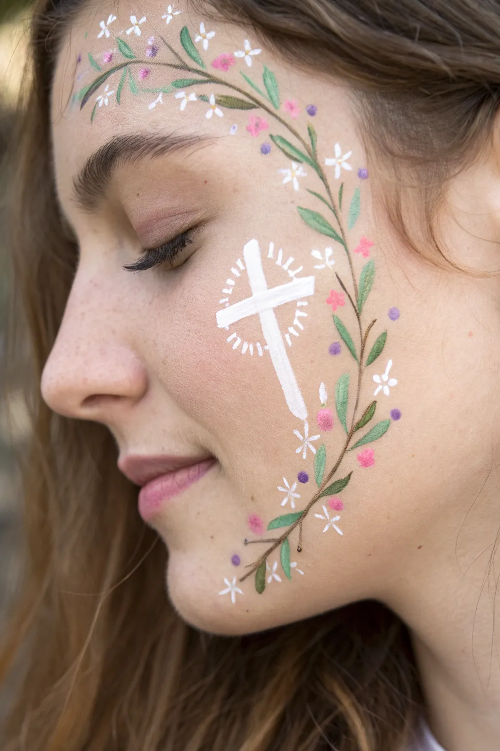 White cross framed by pastel florals on the cheek, minimalist boho face paint with crisp contrast
