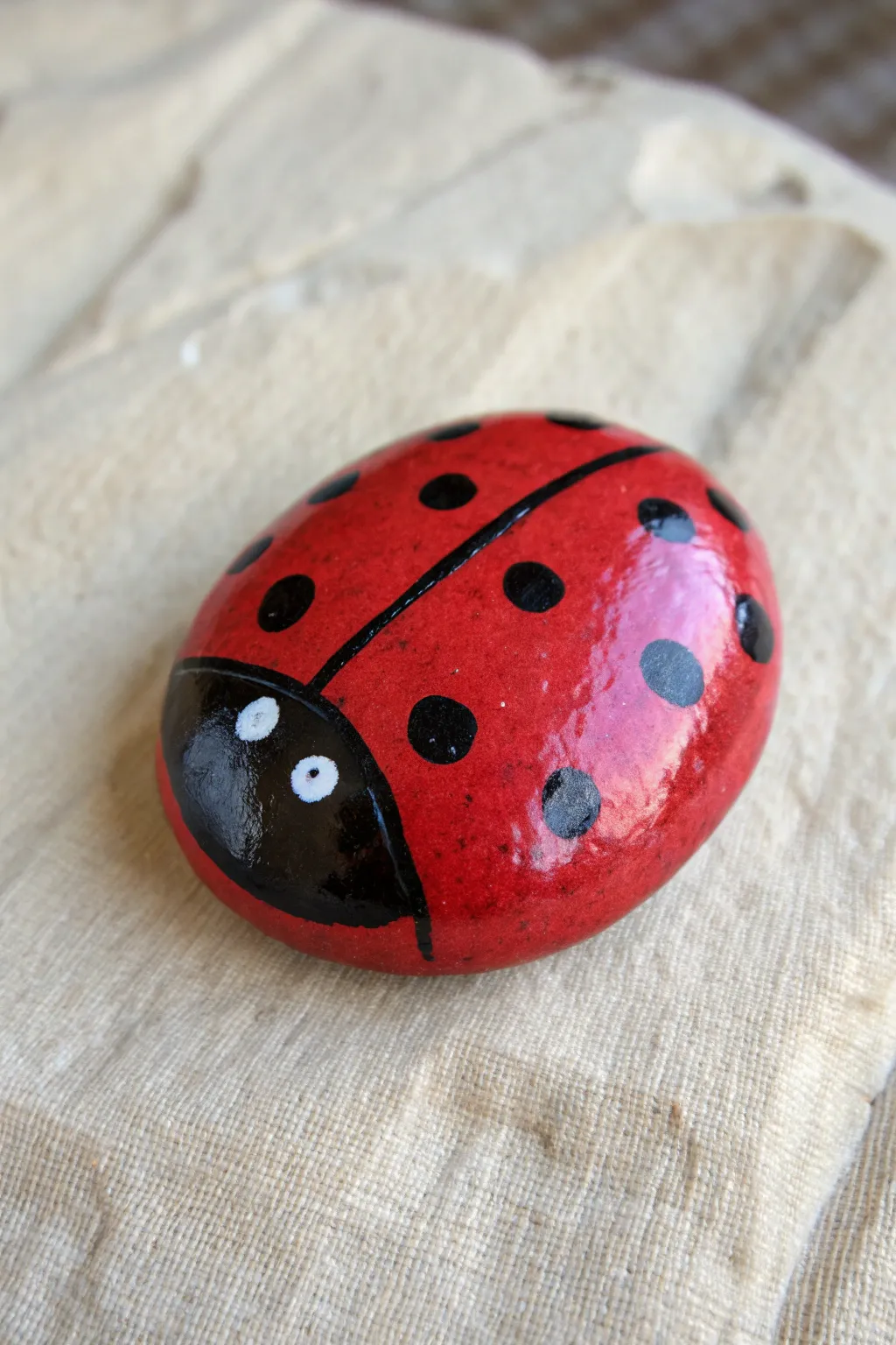 Classic ladybug circle rock with glossy red shine and minimalist spots on soft linen